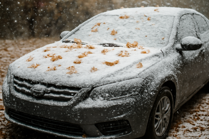 voiture hivernée entourée de feuilles et neige légère